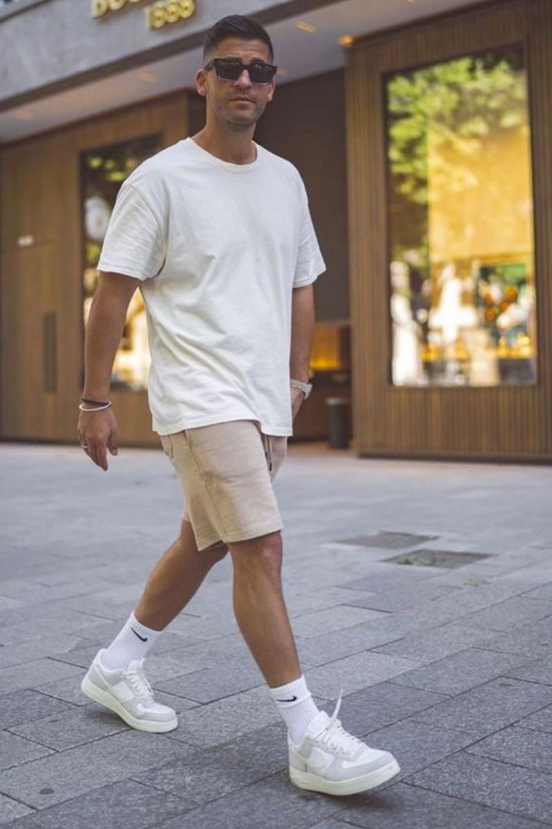 Homem de cabelos curtos usando camiseta branca e bermuda de sarja num look casual masculino descomplicado