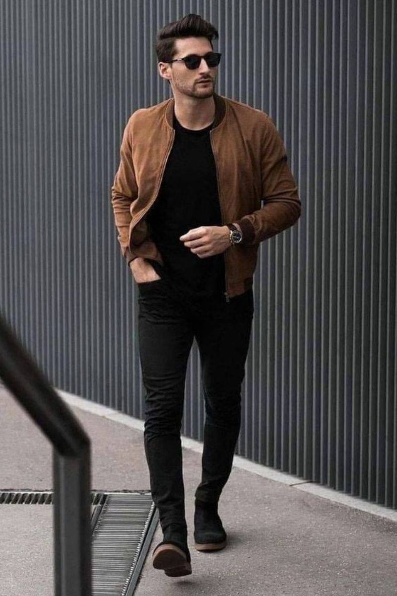 Homem branco usando um look casual masculino all black finalizado por uma jaqueta bomber marrom