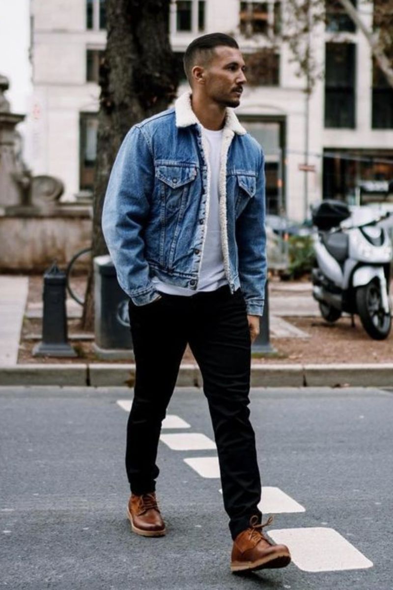 Homem cruzando a rua usando um look casual masculino composto por jaqueta jeans, camiseta branca, calça jeans preta e sapatênis caramelo