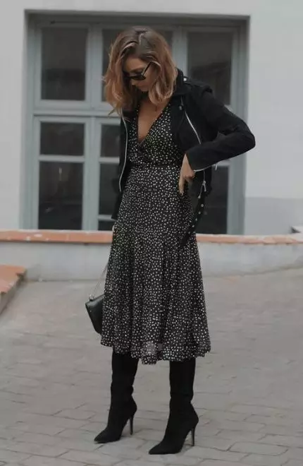 Mulher usando um vestido de bolinhas com uma jaqueta preta e um modelo de bota de cano alto