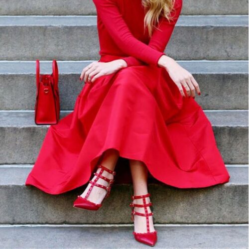 Mulher sentada nas escadas usando um look que responde à pergunta vestido vemelho combina com que cor de sapato?