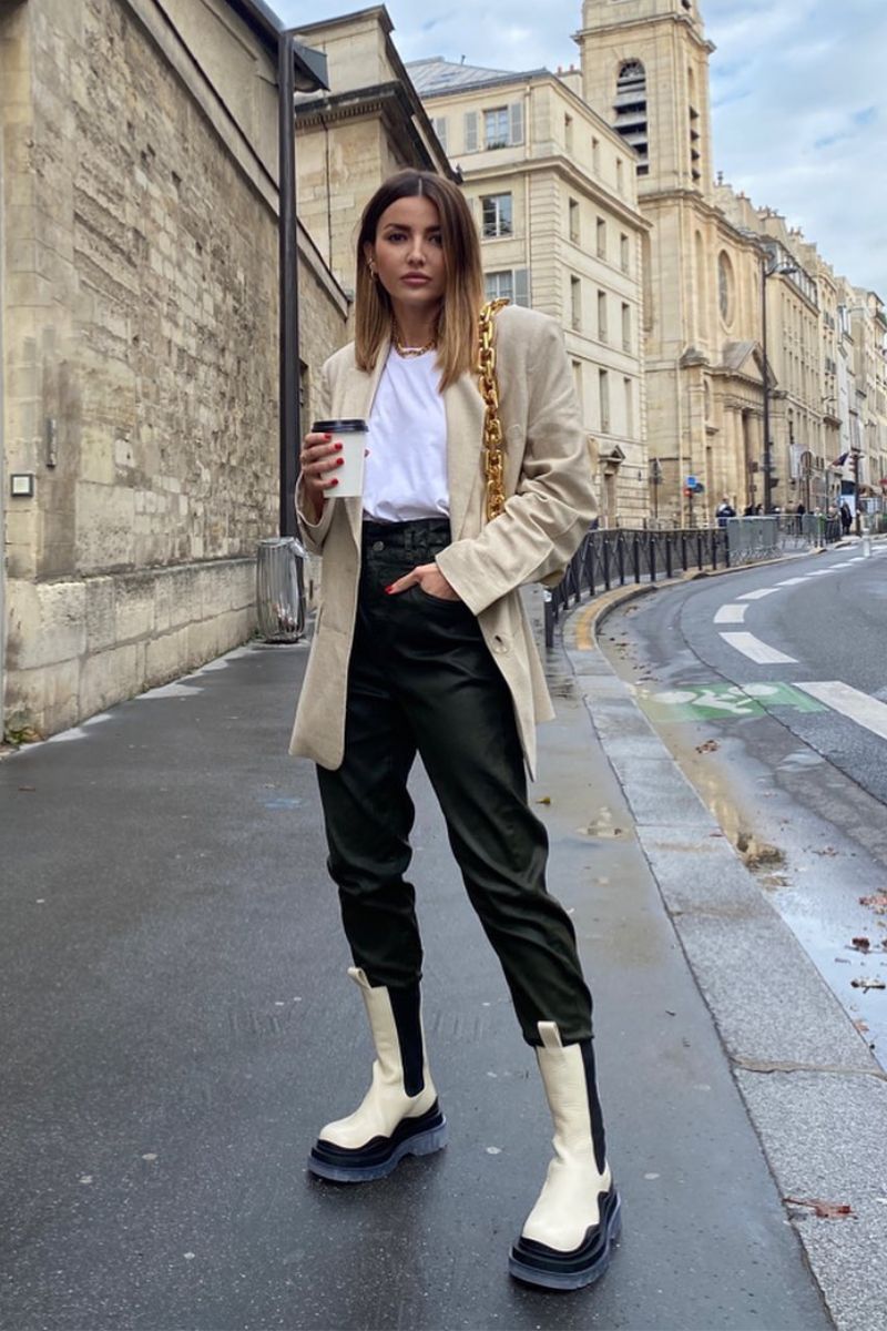 Mulher tomando um café e mostrando como usar bota off white com calça de couro