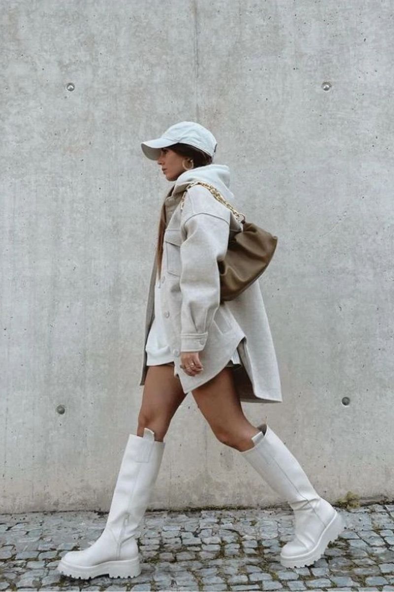 Mulher morena usando um boné branco dando um exemplo de como usar bota off white do estilo chelsea