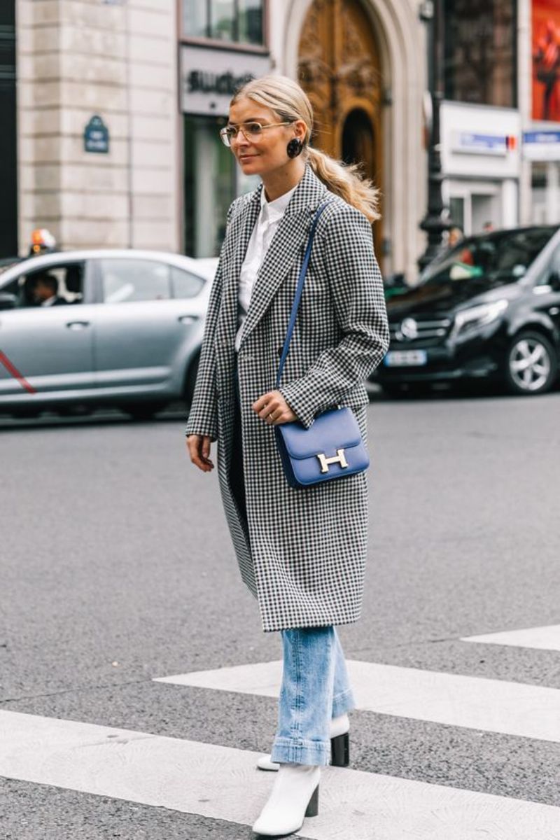 Mulher mostrando como usar bota off white com calça jeans e sobretudo quadriculado