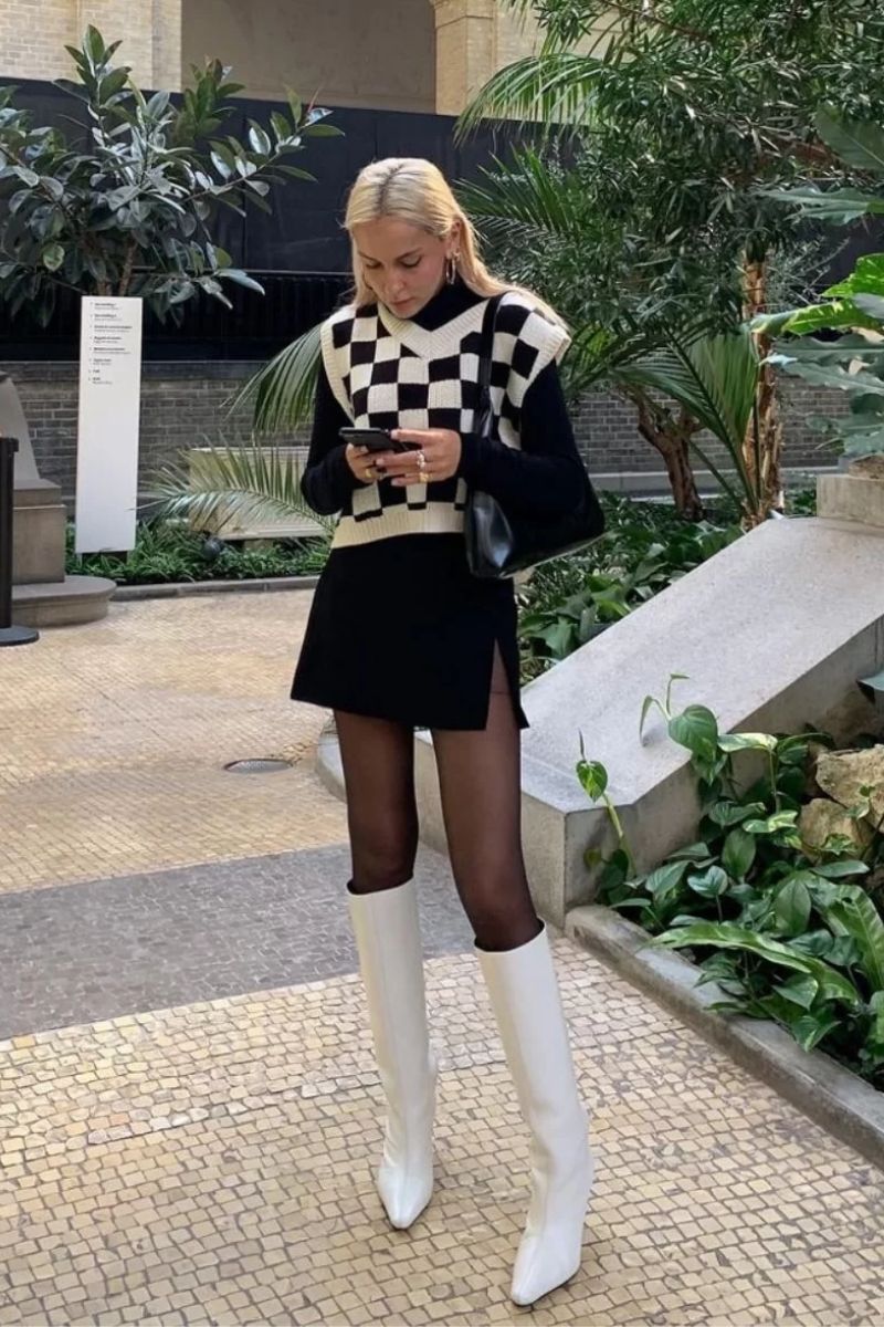 Mulher loira exibindo como usar bota off white com um suéter quadriculado branco e preto e saia preta