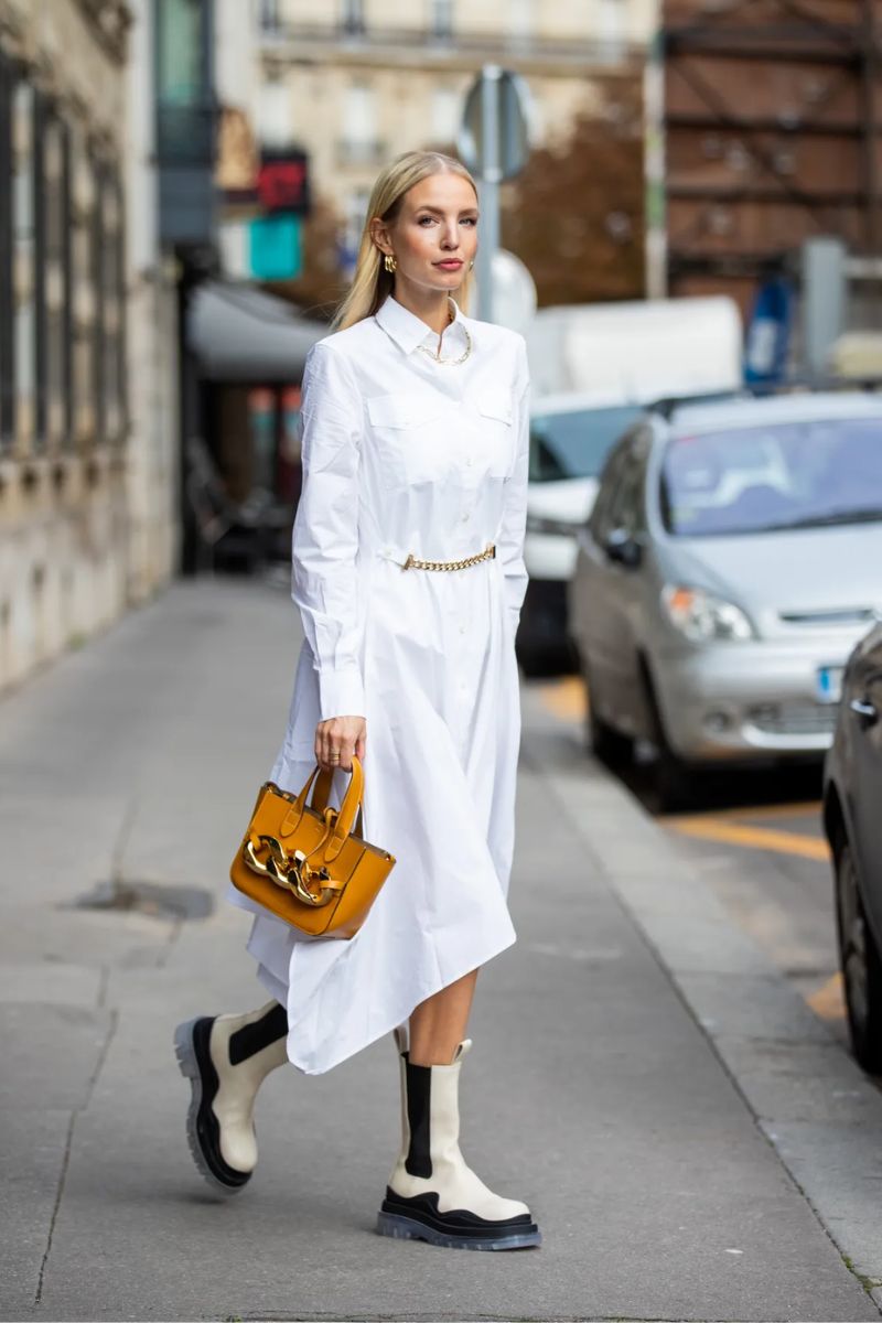 Mulher loira usando um look monocromático branco e uma bota tratorada com uma bolsa contrastante de cor alaranjada