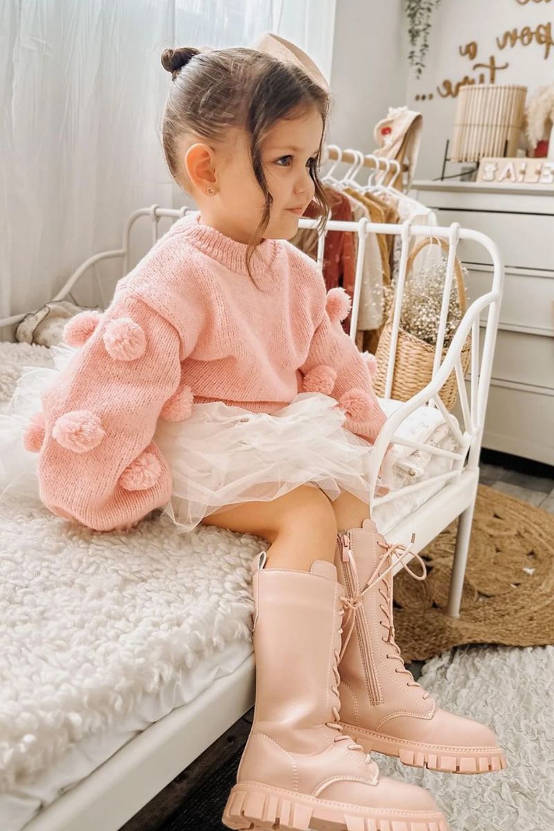 Menina pequena de cabelos presos usando um look infantil com bota composto por saia de tule, blusa felpuda rosa e bota cano longo rosa