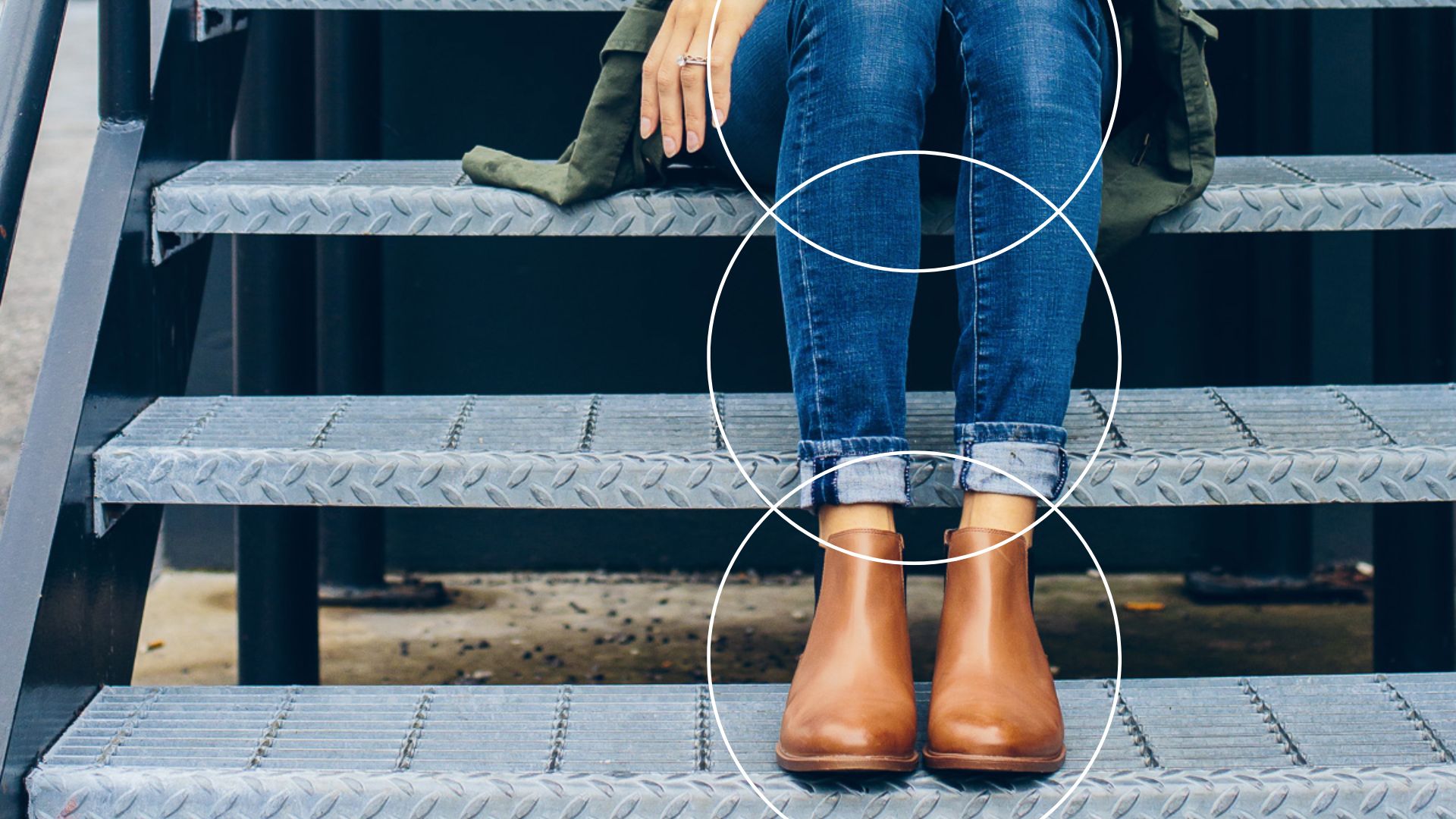 Pernas de uma mulher usando um look com bota marrom cano curto sentada numa escada metálica