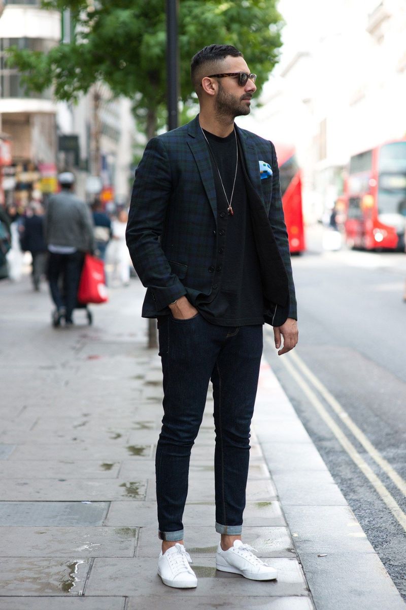 Homem usando um look composto por blazer escuro, calça jeans de lavagem escura e tênis confortável para trabalhar  de estilo casual branco