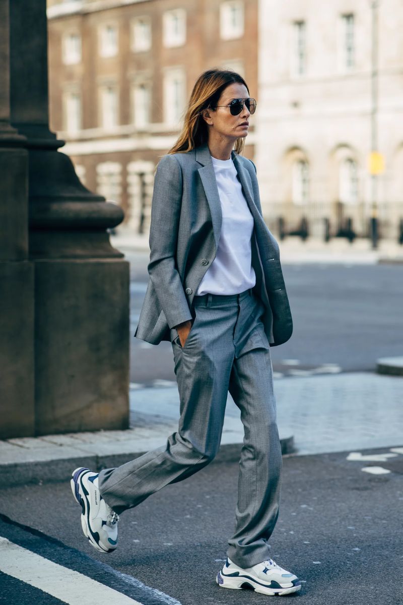 Mulher caminhando usando um blazer, calça social de corte reto, óculos escuros e tênis confortável para trabalhar estilo chunky