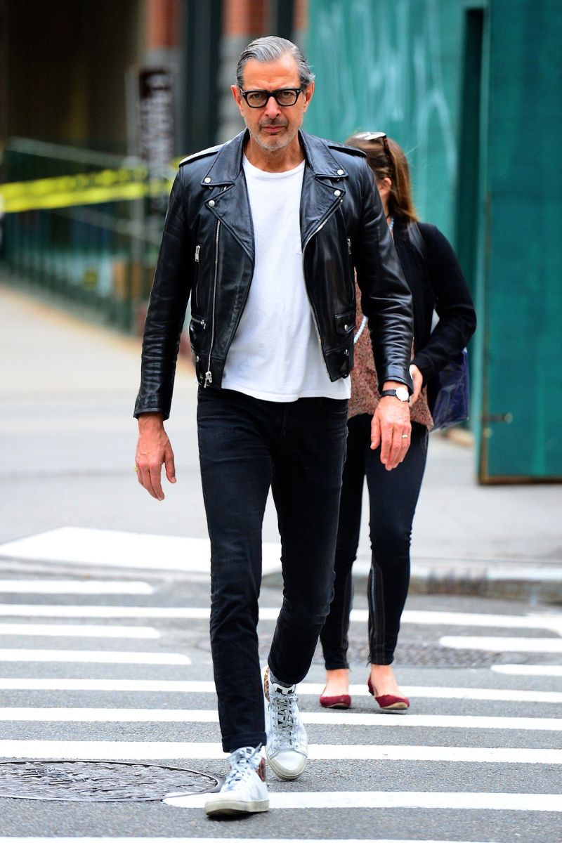 Homem grisalho usando um look composto por jaqueta de couro, camiseta branca, calça jeans de lavagem escura e tênis confortável para trabalhar