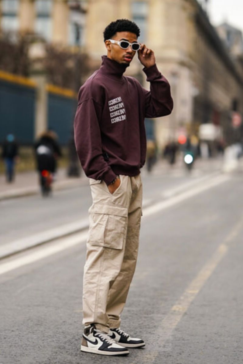 Homem negro usando um look despojado composto por blusa de gola alta e um tipo de calça masculina de estilo cargo clara