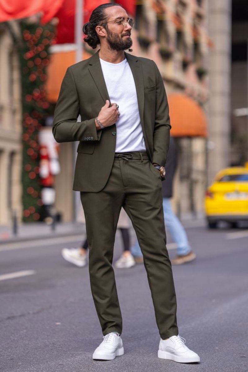 Homem de cabelos longos presos usando um look composto por blazer e um tipo de calça masculina Slim Fit da mesma cor que o blazer (verde escuro)