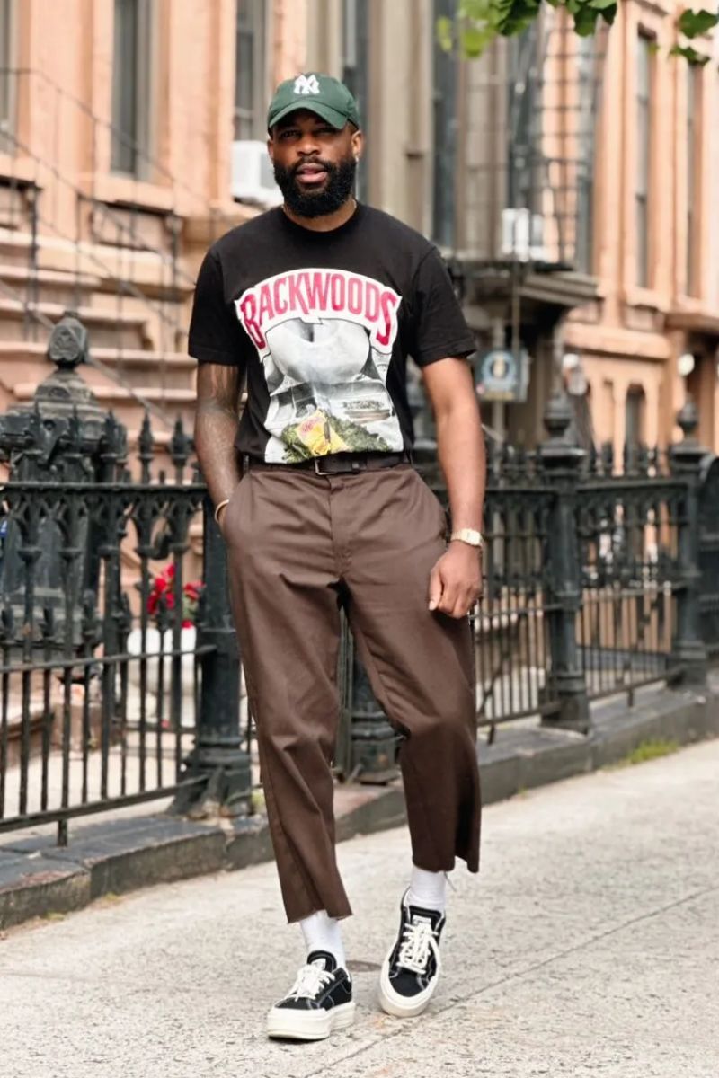 Homem negro usando um look despojado de calça alfaitaria com camiseta estampada e boné