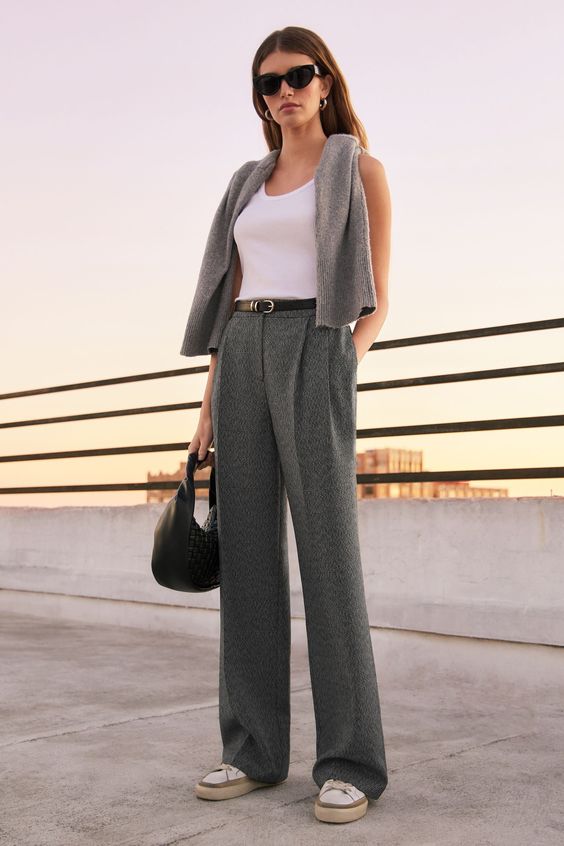 Mulher morena e branca usando um look com calça alfaiataria composto por calça alfaiataria cinza e regata branca