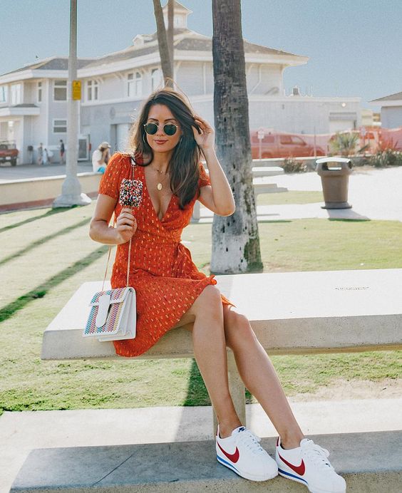 Mulher morena de cabelos soltos usando um look com tênis casual feminino composto por vestido floral e tênis Nike