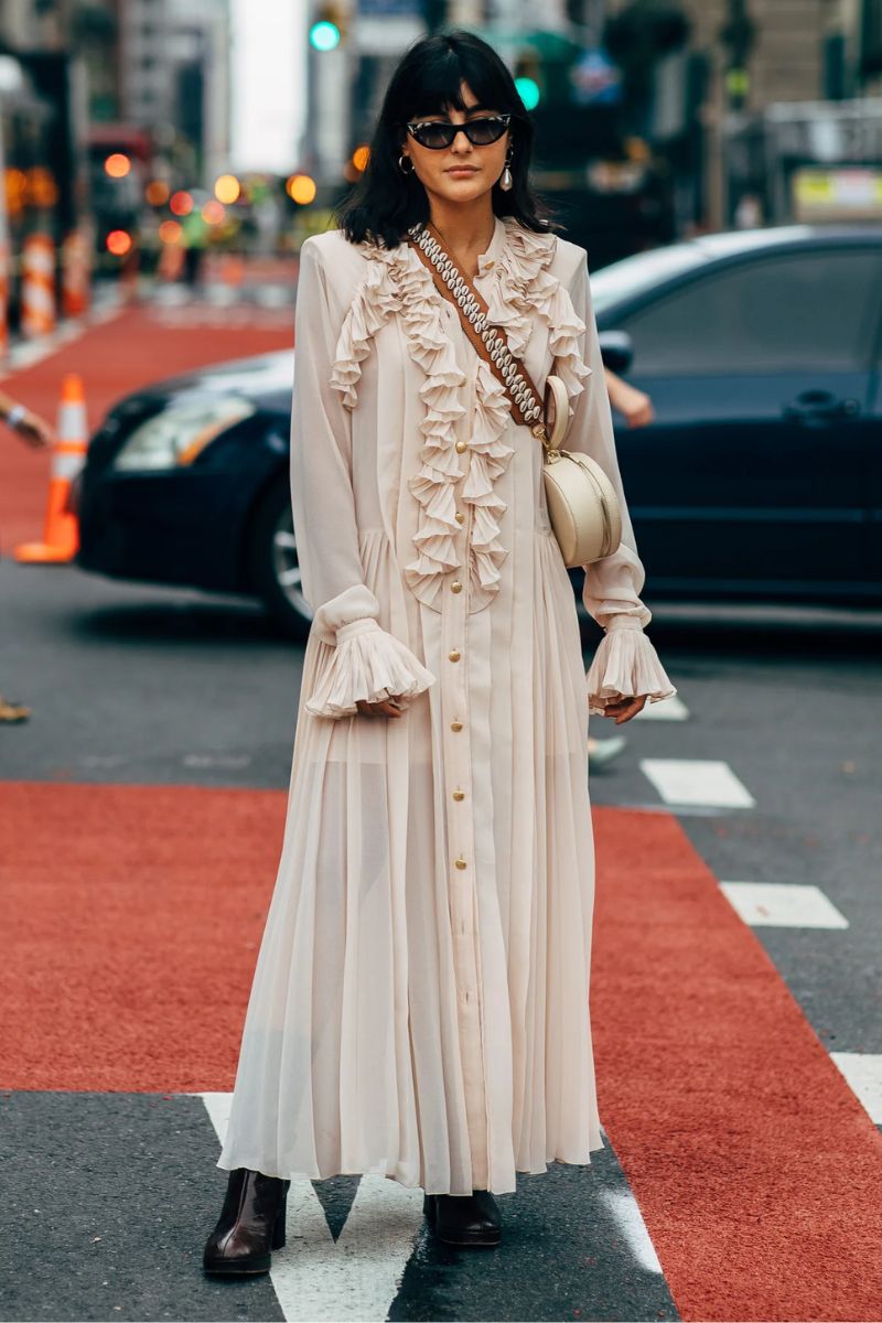 Mulher asiática de cabelos escuros e óculos escuros dando um exemplo de o que é estilo boho com vestido longo