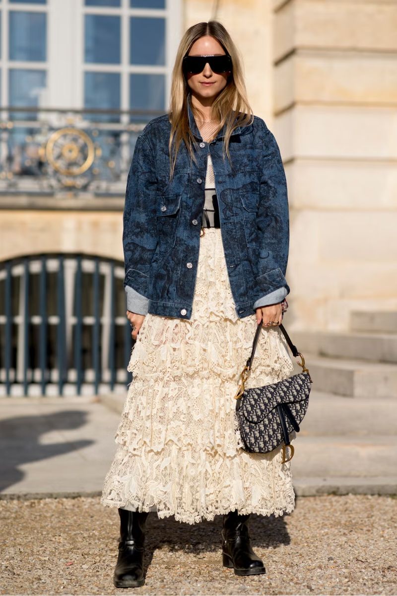 Mulher loira de cabelos soltos e óculos escuros dando um exemplo de o que é estilo boho com jaqueta jeans