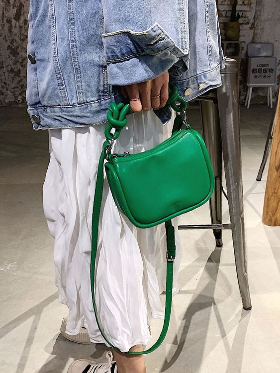 Mulher branca usando um look com bolsa verde usando uma jaqueta jeans e vestido branco