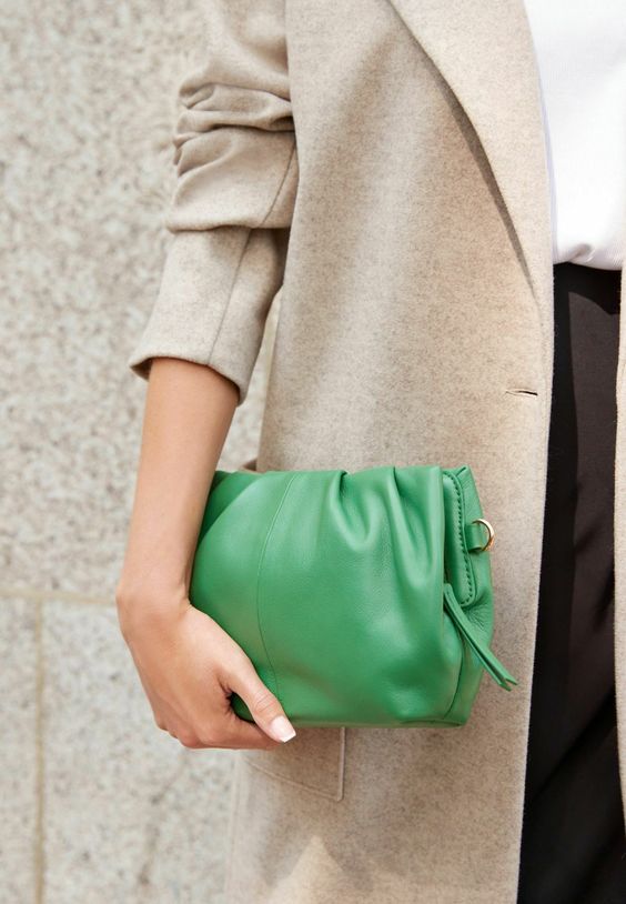 Mulher branca usando um maxxi blazer usando um look com bolsa verde no estilo clutch