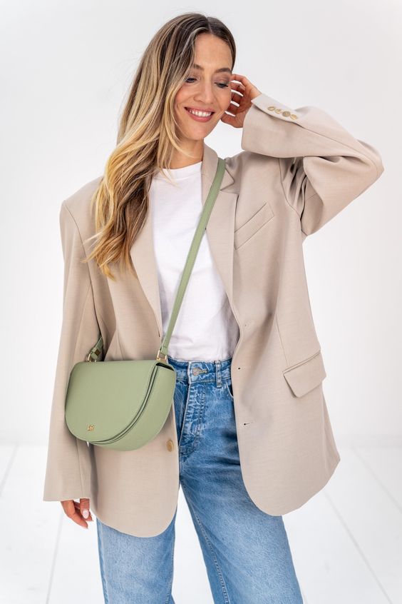 Mulher loira usando um maxxi blazer de cor clara usando um look com bolsa verde no estilo crossbody