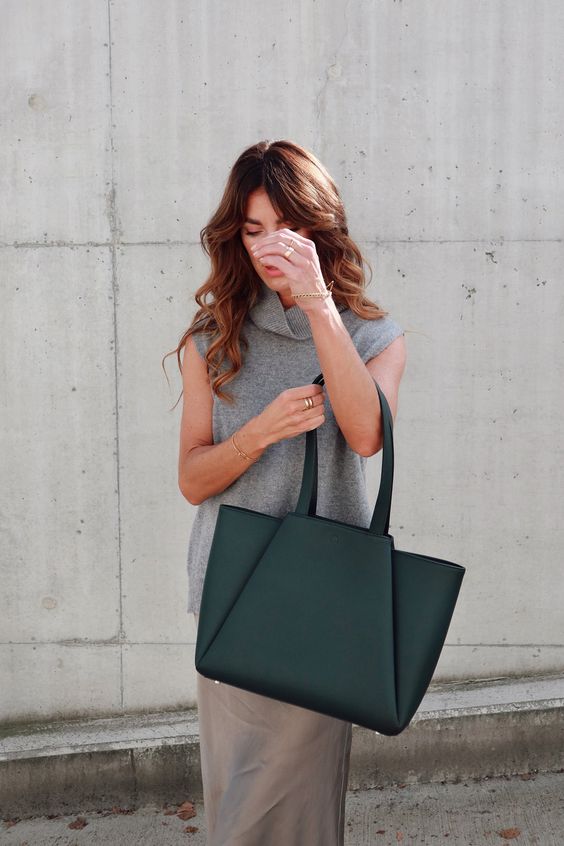 Mulher de cabelos castanhos e ondulados usando um look com bolsa verde no estilo Tote