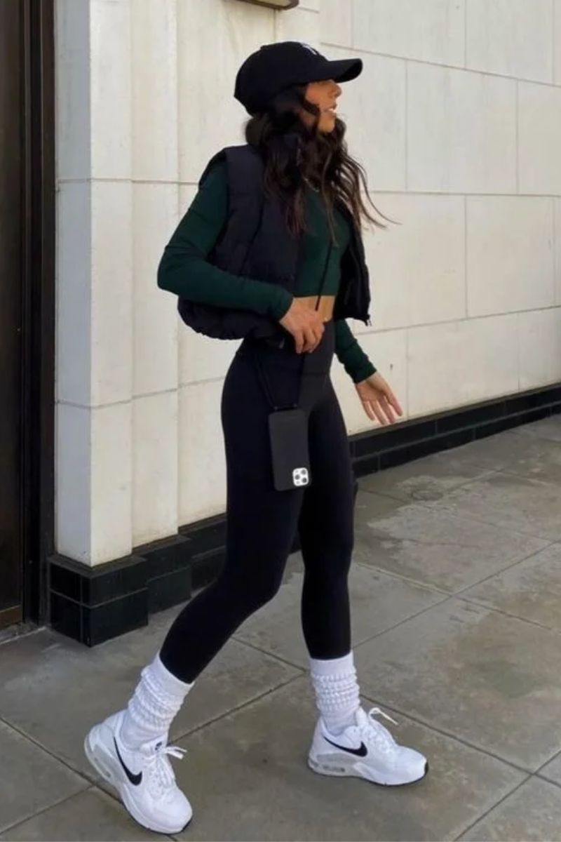 Mulher de cabelos castanhos escuros usando um look para caminhada composto por legging, polainas e jaqueta puffer para caminhar em dias frios