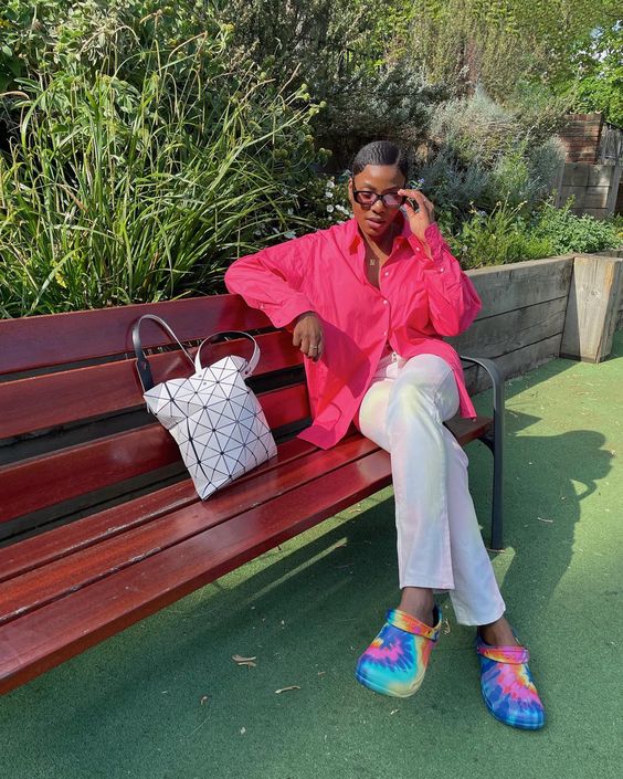 Mulher negra sentada num banco envernizado mostrando como personalizar seu Crocs usando a técnica Tie-Dye