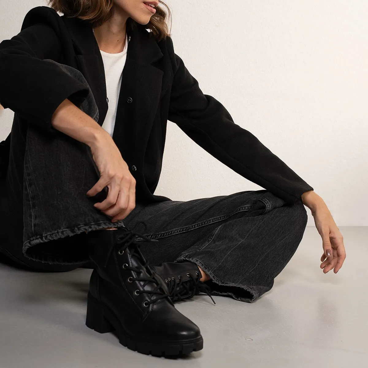 Modelo de cabelos soltos usando roupa preta e camiseta branca. Nos pés ela usa um coturno feminino preto da marca Via Marte